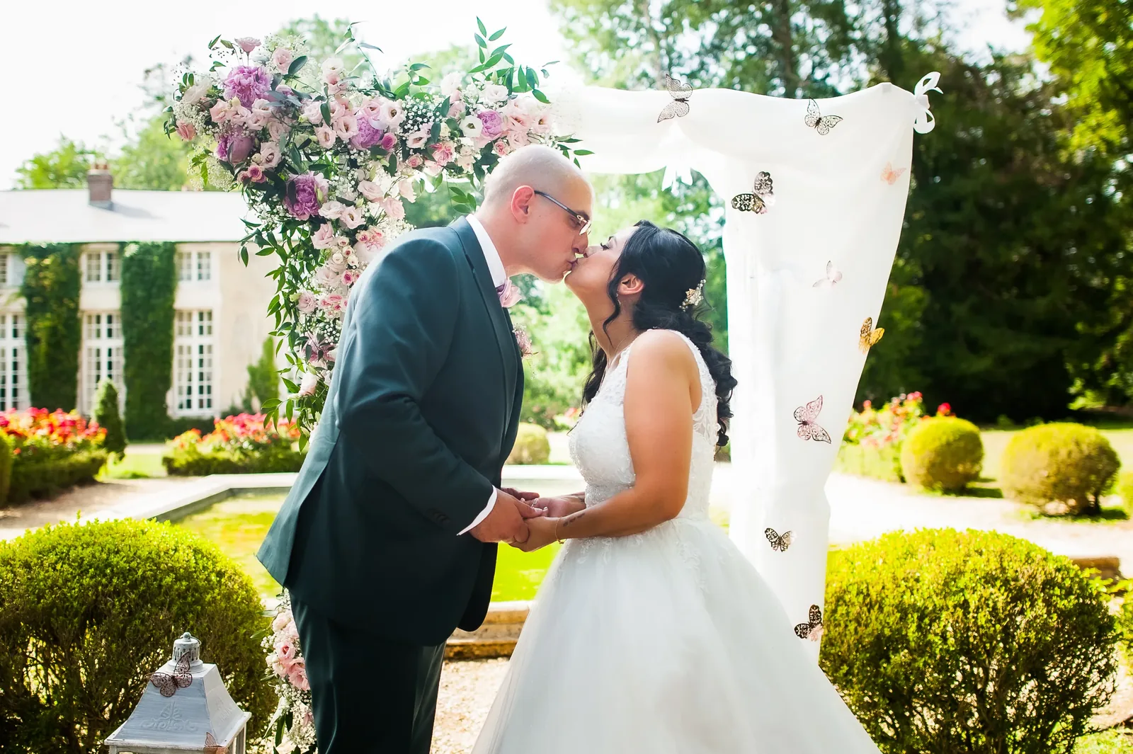 Cérémonie de Sara et Steven : baiser des mariés sous l'arche fleurie, cérémonie laïque officiée par All in Wedding